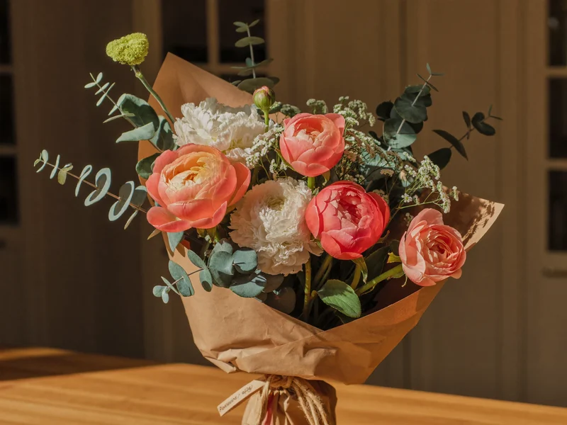 Bouquet stagionale di peonie, ranuncoli ed eucalipto in carta kraft su banco di legno