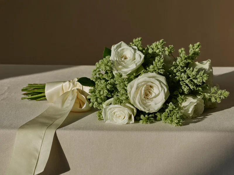 Bouquet da sposa di rose bianche e verde con nastro di seta su lino